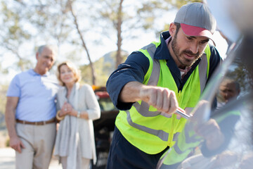Naklejka premium Senior couple watching male roadside assistance mechanic fix car