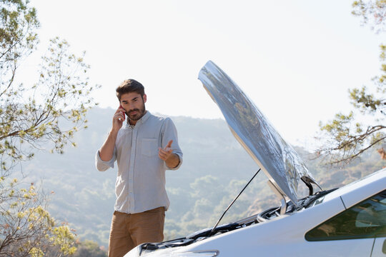Man with car breakdown calling for help at sunny roadside