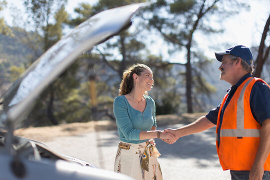 Male roadside assistance mechanic shaking hands with woman at car