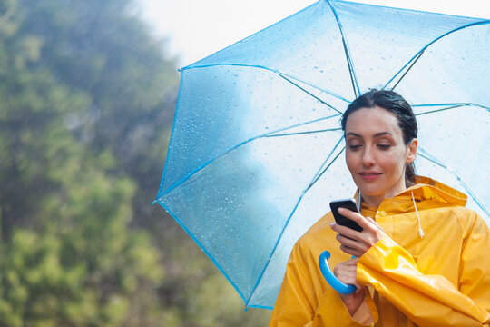 Woman with umbrella using smart phone in rain