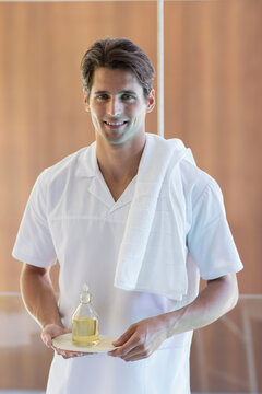 Portrait confident young male masseuse holding massage oil