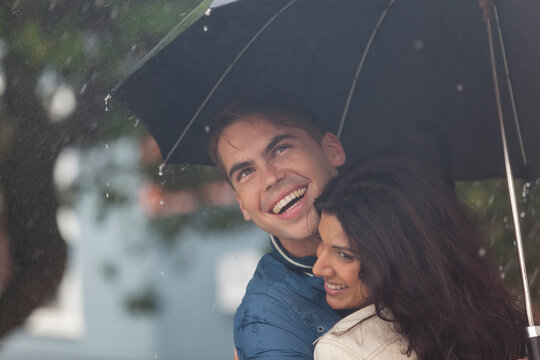 Happy young couple with umbrella in rain