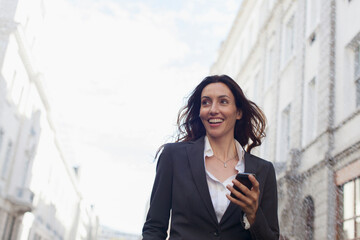 Fototapeta premium Smiling businesswoman with smart phone on city street