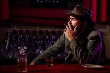 Bearded man smoking cigarette and holding glass of whiskey.