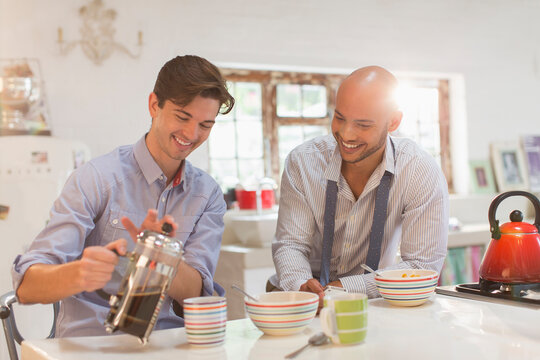 Young male roommates enjoying coffee and cereal in morning kitchen