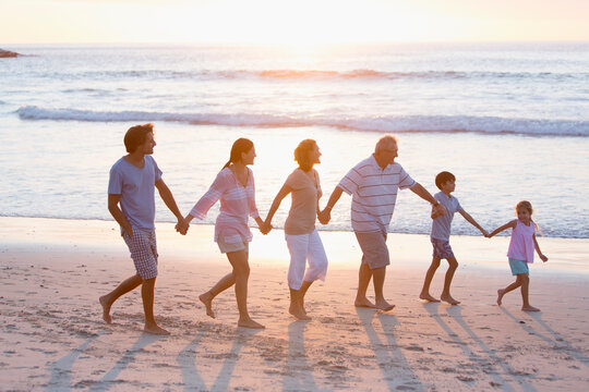 Multi-generation family holding hands and walking on sunny beach
