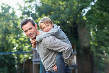 Obraz premium Portrait happy father piggybacking son at playground