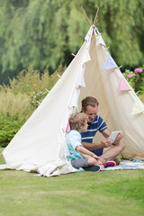 Father and son using digital tablet in teepee in garden © Paul Bradbury/Caia Image