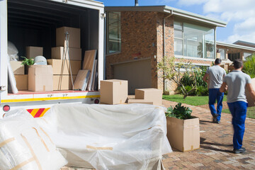 Movers carrying boxes from moving van in sunny driveway © Paul Bradbury/Caia Image