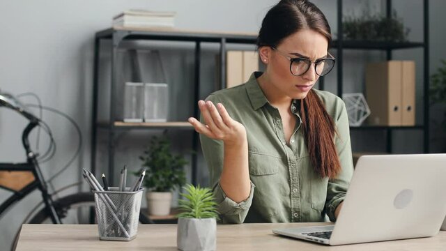 Young beautiful woman with glasses working on laptop. Female worker working hard on computer in modern loft style office.