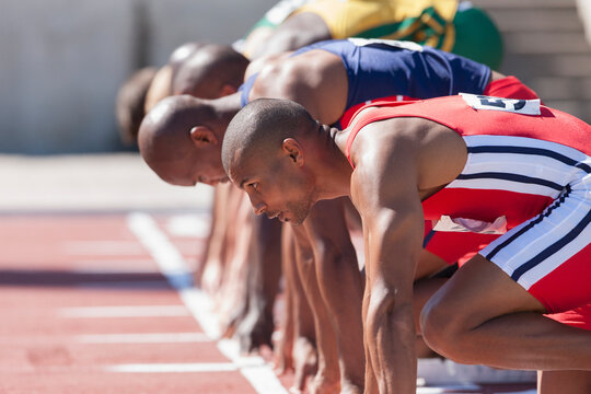 Focused male track and field athletes at sunny starting line