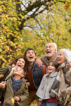 Happy multi-generation family watching falling autumn leaves in park