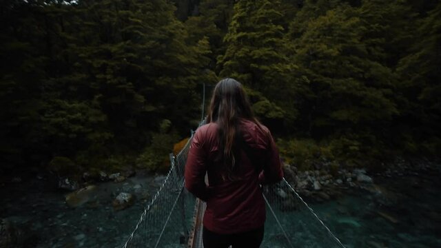 Woman hiking across narrow bridge over river