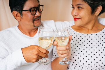 Senior couple sitting on a couch celebrate with wine glass.