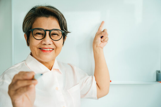 Elderly Senior Old Teacher Woman Standing Near White Board And Pointing At Camera.