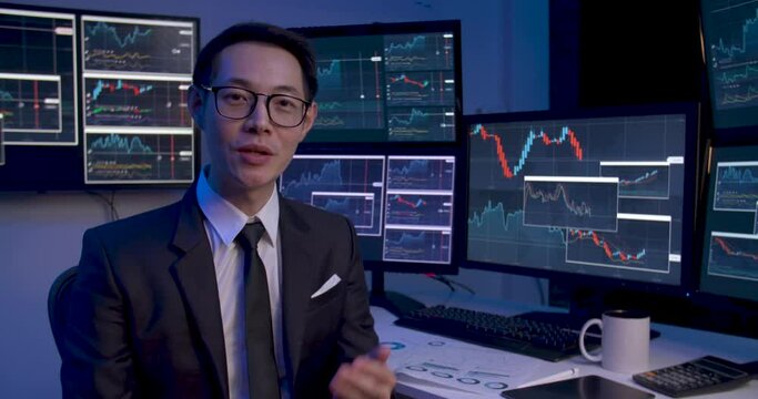 Asian business man is analyzing online stock market trading graph, crypto growth chart with monitors showing on screen. Alone male video conference of financial strategy at late night. Web cam view.