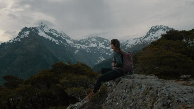 Woman Hiker Sitting On A Mountaintop Surrounded By Mountain Peaks