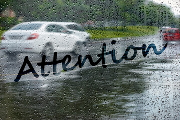 Defocused traffic through wet glass and text Attention on it