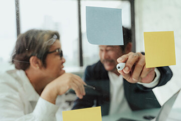 Senior business people pointing at sticky note.