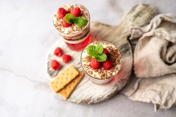 Dessert in a glass cup, with Jello covered in yogurt and topped with fresh raspberries. Mini dessert on light concrete background. Fruit parfait with jello and jelly. 