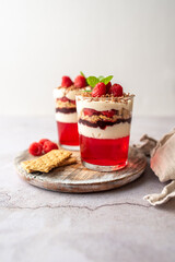 Dessert in a glass cup, with Jello covered in yogurt and topped with fresh raspberries. Mini dessert on light concrete background. Fruit parfait with jello and jelly. 