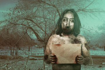 Scary zombie with blood and wound on his body holding an empty board on the field