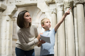 Young woman with son observing with interest sculptures exhibition in art museum, pointing to...