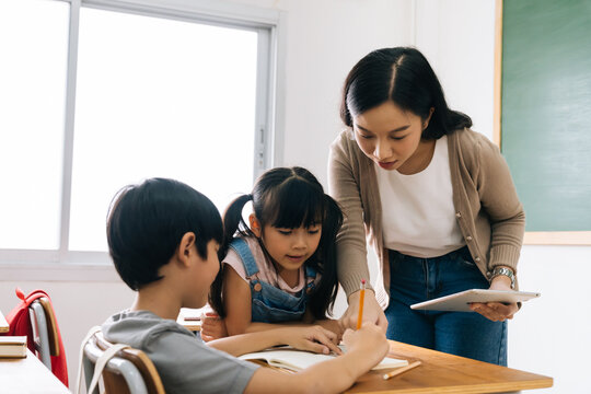 Asian School Teacher Using Digital Device With Children In Classroom At School, Technology, Learning, Development.