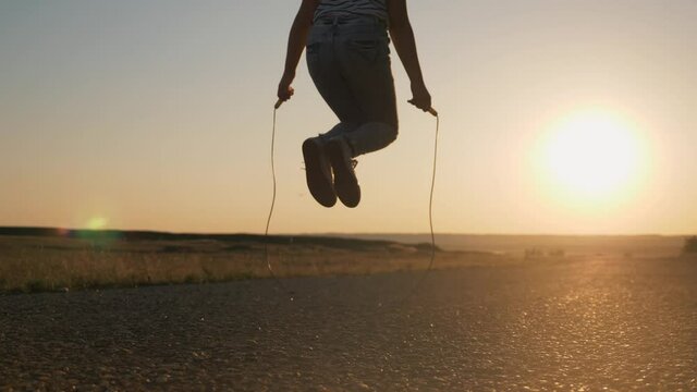 Girl jumping rope in the rays of the sun. Child's legs jumping rope skipping rope closeup silhouette. The kid plays sports games. Healthy lifestyle. Happy kid in the park