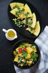 Yellow watermelon and herbed cucumber salad, flatlay over black stone background, vertical shot