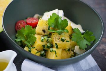 Salad with yellow watermelon cubes, herbed chopped cucumber, cheese and fresh parsley served in a green bowl, close-up, selective focus