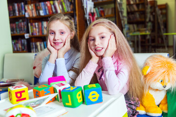 Fototapeta premium Two funny girls playing with alphabet blocks in the library