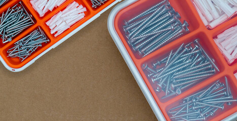 Steel silver screws and wall plug in orange plastic box. Top view tool box on brown paper box background with copy space. Set of screws and plastic plug for drilling wall and installation things.