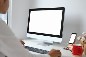 Fototapeta premium Cropped shot of young man working with computer and smart phone with white screen on work space.