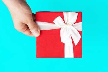 A man's hand holds a red box with a white ribbon on blue background.