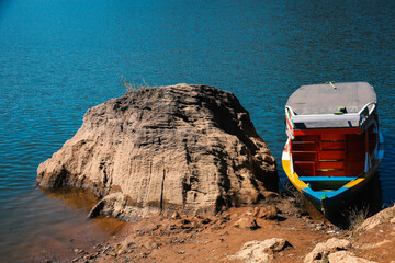 Colorful wooden boat parking on the lake beside the big rock. Beautiful lake scenery 