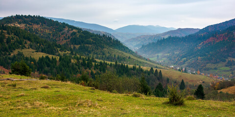 Obraz premium foggy morning in carpathian countryside. village down in the rural valley. trees in fall foliage on the hills. gloomy weather