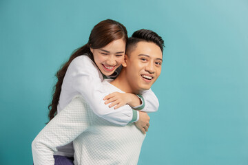 Piggyback ride. Young man carrying girlfriend on his back, blue background with copy space.