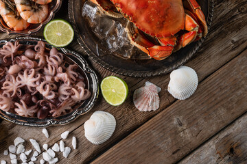 Top view of plates with cooked crab, octopuses and large shrimps served with lime, seashells and sea salts on wooden rustic background. Seafood concept. Organic food. Italian cuisine.