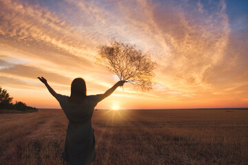 Fototapeta premium The girl raised her hands up to meet the sunset in her hand flowers. Romantic mood, beautiful sunset