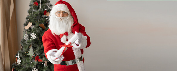 Santa Claus holds out a rolled paper roll in his hands. Obedient children list concept.