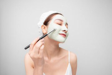Happy young Asian woman applying clay mask on her face isolated over white background. Beauty, skin care concept.