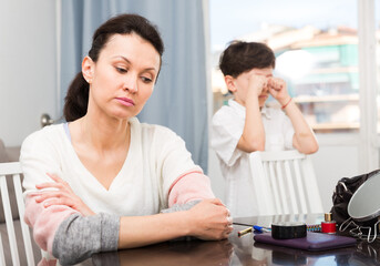 Portrait of offended mother after disagreements with preteen son sitting at home