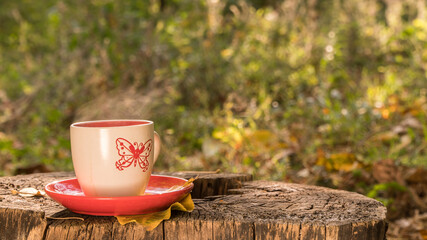 a cup of coffee stands on a wooden surface next to yellow leaves