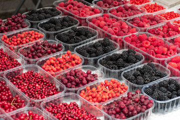 Red and black fresh healthy berries, cranberries, lingonberries, raspberries, blackberries in a small baskets in a street food market ready to sell and eat