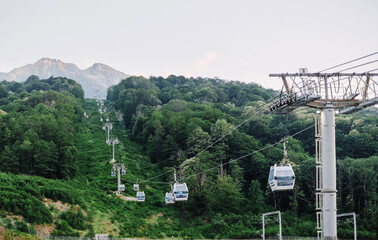 Esto-Sadok, Sochi, Russia. Cableway among lush green forest in summer mountains in front of Aibga ridge on resort Gorky Gorod, Krasnaya Polyana.