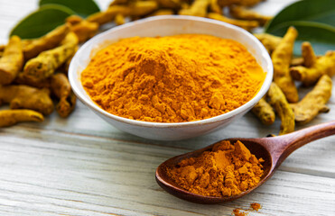 Bowl with turmeric powder and dry roots on a wooden background