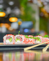 Salmon and caviar sushi rolls served on a traditional plate on a wooden table in a restaurant.