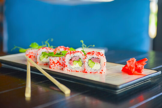Salmon and caviar sushi rolls served on a traditional plate on a wooden table in a restaurant.