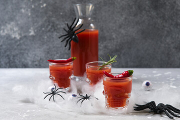Bloody Mary cocktail or tomato juice in glasses shaped like skulls, Halloween decor cobwebs,...